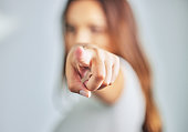 Studio shot of a young woman pointing forward against a grey background.
