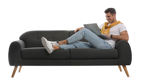 Man with laptop on comfortable grey sofa against white background