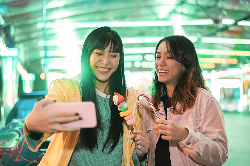 Happy asian girls having fun doing selfie outdoors at amusement park - Focus on faces