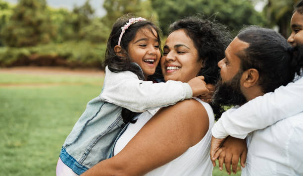 屋外で楽しいインドの家族 - 都市公園で子供と一緒に笑っているヒンズー教の両親 - 愛の概念 - 母と娘の顔に主な焦点 - インド人 ストックフォトと画像