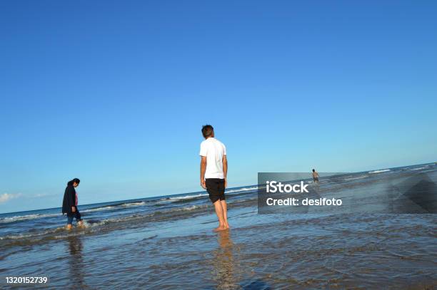 A Senior Man Standing Barefoot At The Beach In Water With His Back Towards Camera A Woman And A Child Are In The Hindsight Stock Photo - Download Image Now