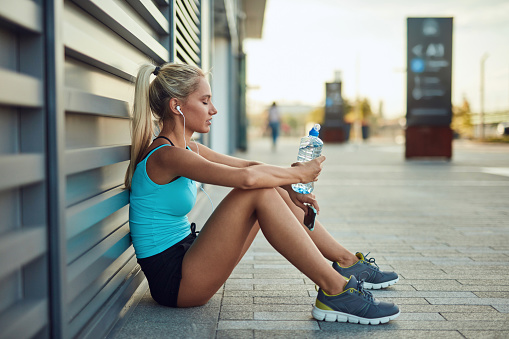 Young blonde sportswoman making pause after jogging and exercising in urban environment.