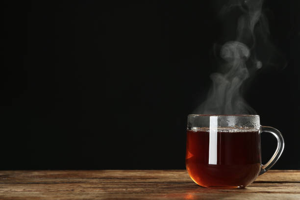 istock Cup with steam on wooden table against black background. Space for text 1320158955