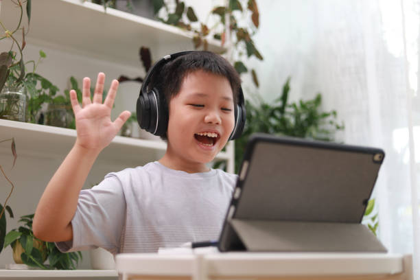Boy studying at home e-learning Close up of a young Asian boy studying and doing homework using his tablet computer and headphones during the pandemic lockdown. male chinese student stock pictures, royalty-free photos & images