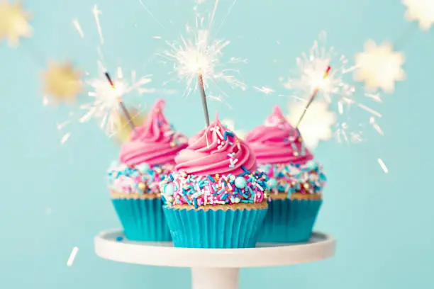 Three birthday cupcakes with pink frosting and party sparklers