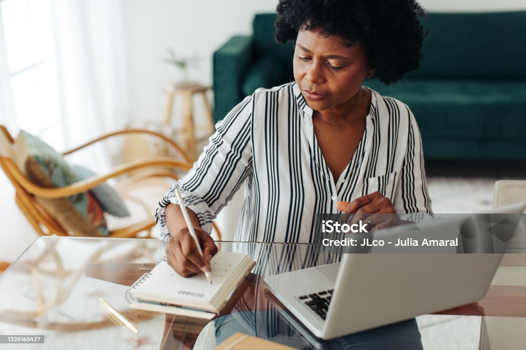 African woman working from home Woman sitting at table and taking notes at home office. African woman working from home. Senior Adult Stock Photo