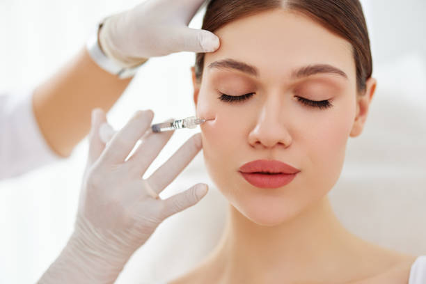 Cosmetician applying filler injection to patient Young female patient getting injection to cheekbone from professional cosmetologist in mask and gloves in beauty procedure in modern clinic botulinum toxin injection stock pictures, royalty-free photos & images