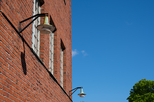 Helsinki / Finland - MAY 22, 2021: A vintage gas powered lamppost hanging on a red brick wall against bright blue sky.