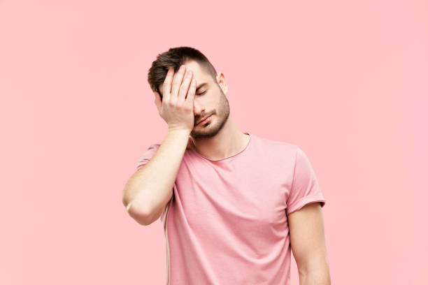 Tired disappointed young man with face palm gesture over pink background stock photo