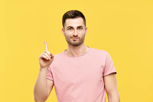 Young funny man pointing his finger up indicates to copy space isolated on yellow background. Presenting product and advertising concept