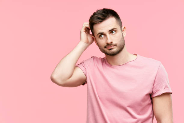 istock Young pensive man have doubts while scratching head looking to copy space on pink background 1320168171
