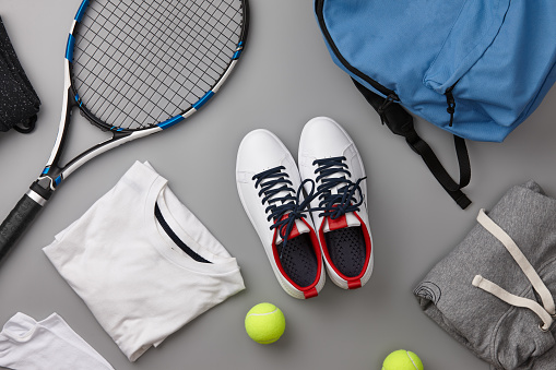 Tennis racket and garments on gray background, top view