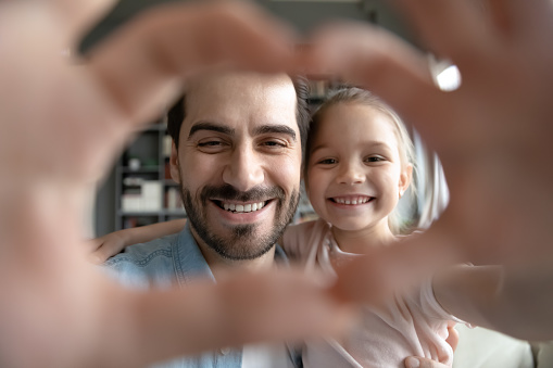 Head shot close up happy young caucasian father and playful cute small child daughter making heart symbol with fingers, enjoying spending free time together at home, loving family relations concept.