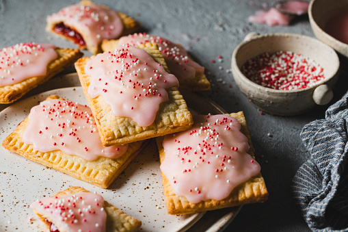 Close-up of freshly baked homemade strawberry pop tarts with multicolored sugar sprinkles served in a plate.