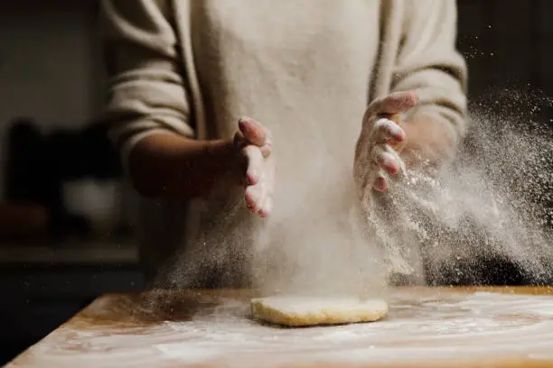 Close-up of a female sprinkling flour on dough over kitchen coutner. Female preparing pastry tarts.