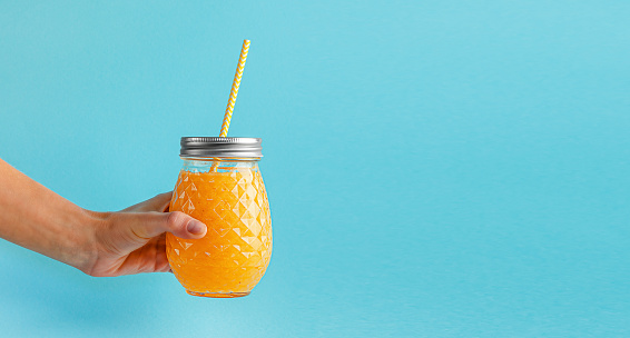 Female hand holding fresh smoothie jar on blue background. Healthy eating, copy space.