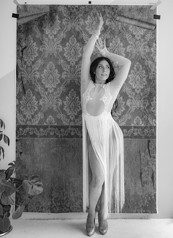 Young Middle eastern woman posing against damask pattern backdrop.She is wearing stage costume. Interior studio shot in black and white.