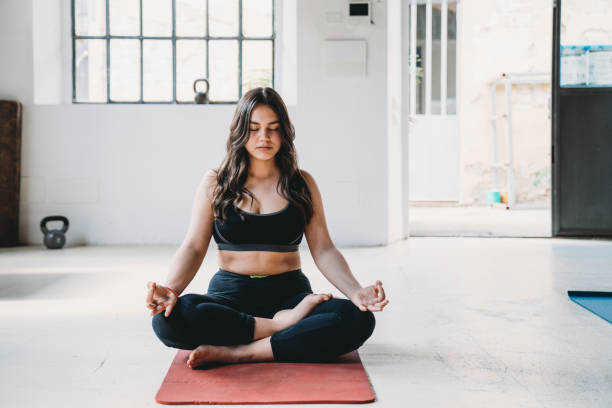 Young adult woman is practicing yoga in a modern loft Young adult woman is practicing yoga in a modern loft. Half lotus or ardha padmasana pose. sukhasana stock pictures, royalty-free photos & images