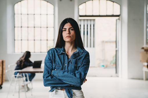 Portrait of a young woman in a modern loft. Other people in the background. Caucasian ethnicity.