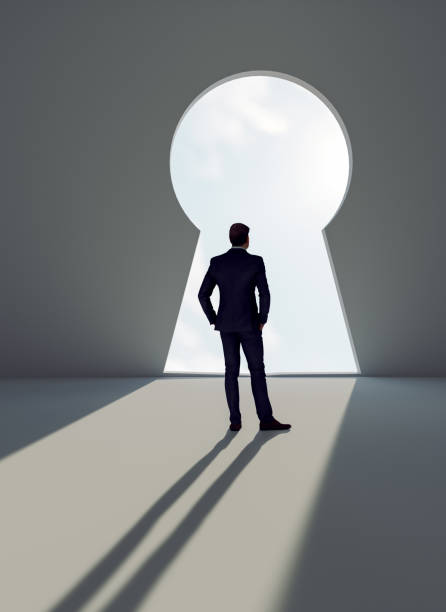 istock Man stands before a key decision and faces a wall with giant key hole 1320180766