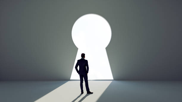 istock Man stands before a key decision and faces a wall with giant key hole 1320180772
