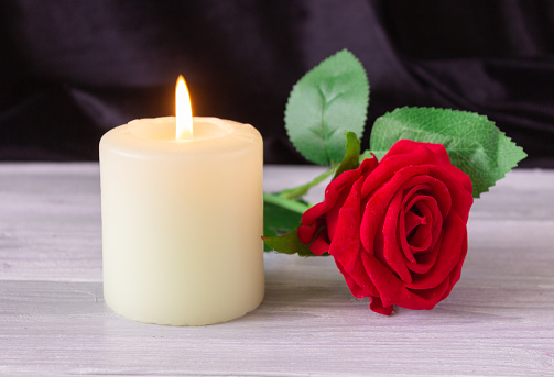 The concept of remembrance, funerals, and condolences. Candle and red rose on black background, free space for text