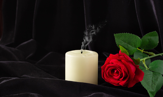 An extinguished candle and a red rose on a black background. The concept of mourning, condolences, funerals.