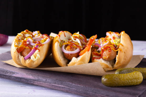 perritos calientes con verduras, mostaza y ketchup en una tabla de cortar, vista lateral comida rápida, comida callejera. - perrito caliente fotografías e imágenes de stock