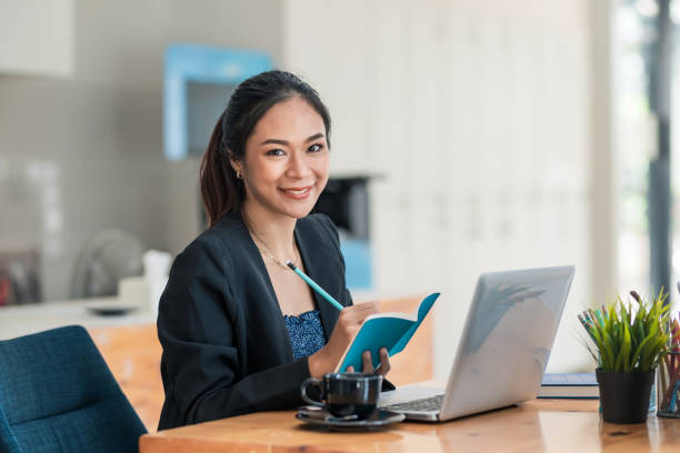 joven empresaria asiática sentada en su escritorio y tomar notas usando la computadora portátil en la oficina. - secretary fotografías e imágenes de stock