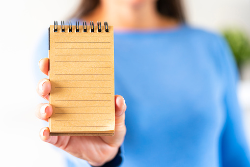 Close up view of a female hand holding a blank brown note pad in front of her. Selective focus on foreground. Copy space.
