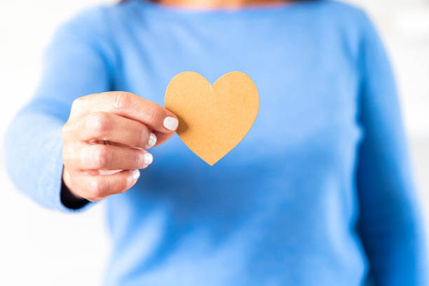 Close up view of a female hand holding a blank brown heart shape in front of her. Selective focus on foreground. Copy space.