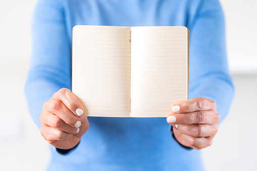 Close up view of a female hand holding an open blank striped note pad in front of her. Selective focus on foreground. Copy space.