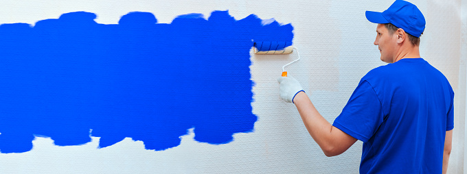 Banner construction and repair. A man in uniform paints the wall inside the room in blue with a paint roller. A blank with space to copy. mockup