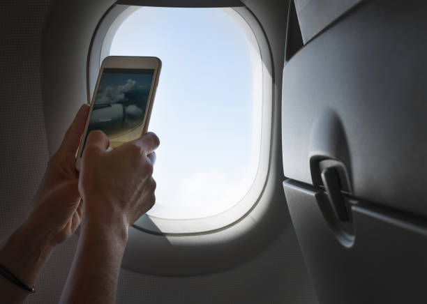 istock Female using her smartphone for photographing clouds and aircraft engine through the porthole. Active traveling and flying by planes aviation transport concept image. 1320192683