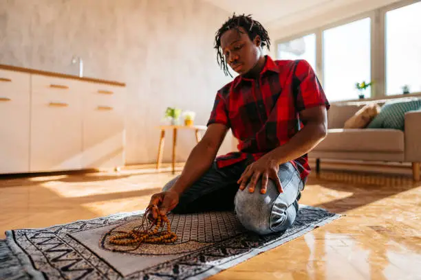 Young African-American Muslim man is praying at home.