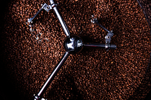 The process of roasting a batch of high quality single origin coffee beans in a large industrial roaster; the toasted beans are in the cooling cycle.