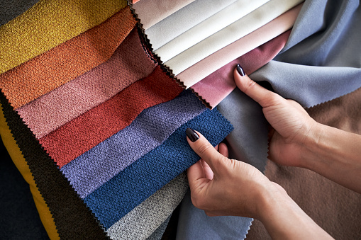 La elección del color y la textura de la tela de tapicería de varias muestras coloridas en una tienda. Manos de cliente femeninas tocando textil. photo