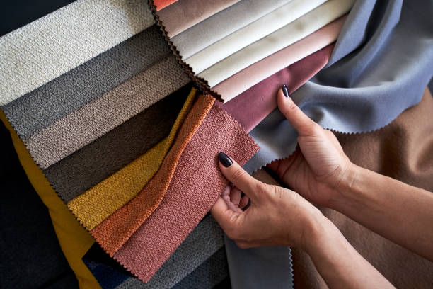 istock Choosing upholstery fabric color and texture from various colorful samples in a store. Female customer hands touching textile. 1320207211