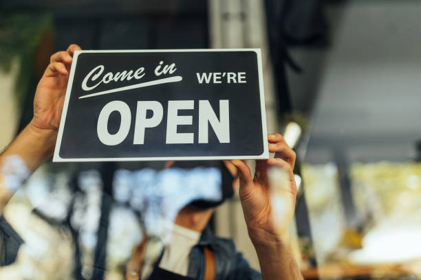istock Business must carry on again. Man posting Open sign on store window 1320207221