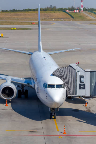 avion blanc relié à la passerelle d’embarquement des passagers - airport window outdoors airfield photos et images de collection
