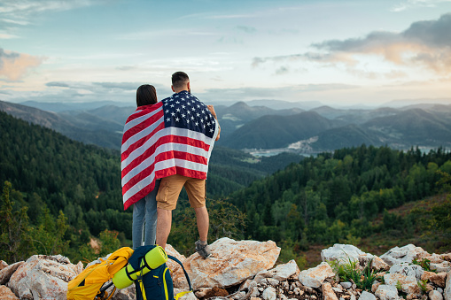 Couple standing on the top of a mountain and holding the American flag