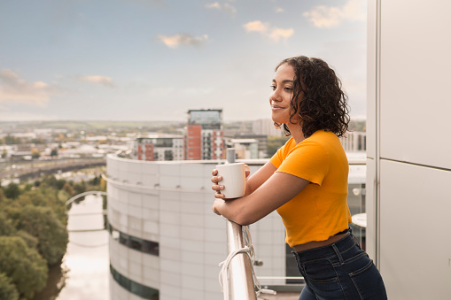Happy young woman on balcony with a coffee, admiring the view