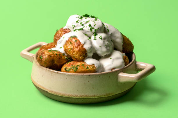 Baked potatoes with sour cream in a tray on a green table. Delicious baked potatoes with sour cream sauce in a ceramic bowl on a green table. Baby potatoes oven-baked with yogurt sauce and herbs. baked potato sour cream stock pictures, royalty-free photos & images