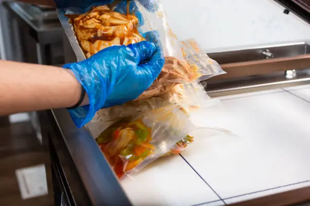 A view of a person using a vacuum packing machine, used in the industry to seal plastic bags of food. Bags of meal prep are being prepared.