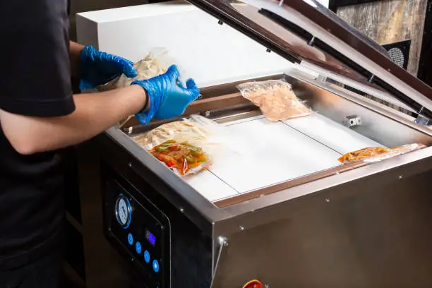 A view of a person preparing plastic sealed food bags in vacuum chamber sealer appliance.