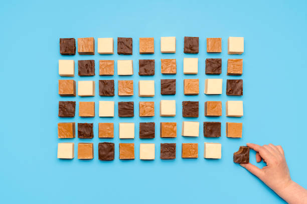 assortimento fudge allineato simmetrico su tavolo blu. donna che afferra caramelle al cioccolato, vista dall'alto - knolling concetto foto e immagini stock