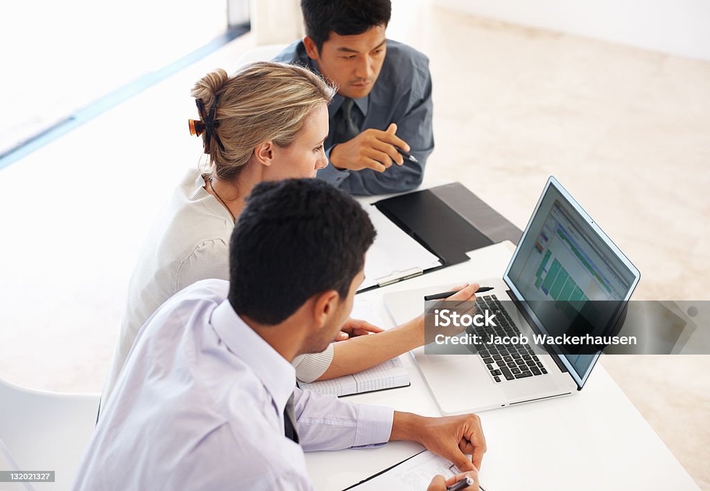 Business team busy at work Confident female executive using laptop while discussing work ideas with male colleagues Adult Stock Photo