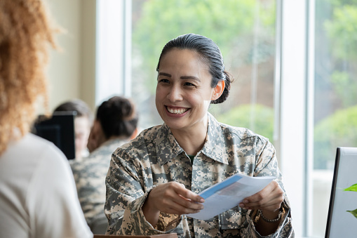 Confident female soldier shows brochure to woman in recruitment office