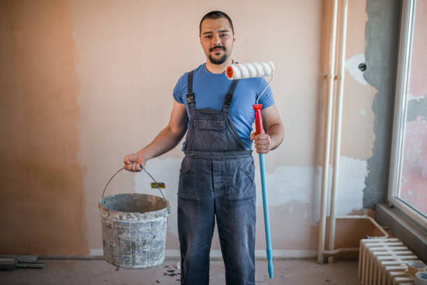 istock Smiling painter in coveralls holding paint roller and a bucket 1320214525