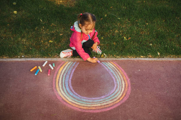 istock Girl drawing a rainbow with chalk on the sidewalk 1320219024
